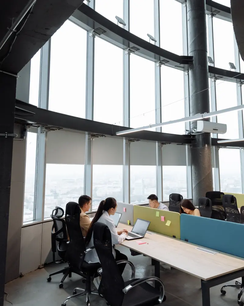Een team aan het werk achter laptops in een kantoor met hoge ramen